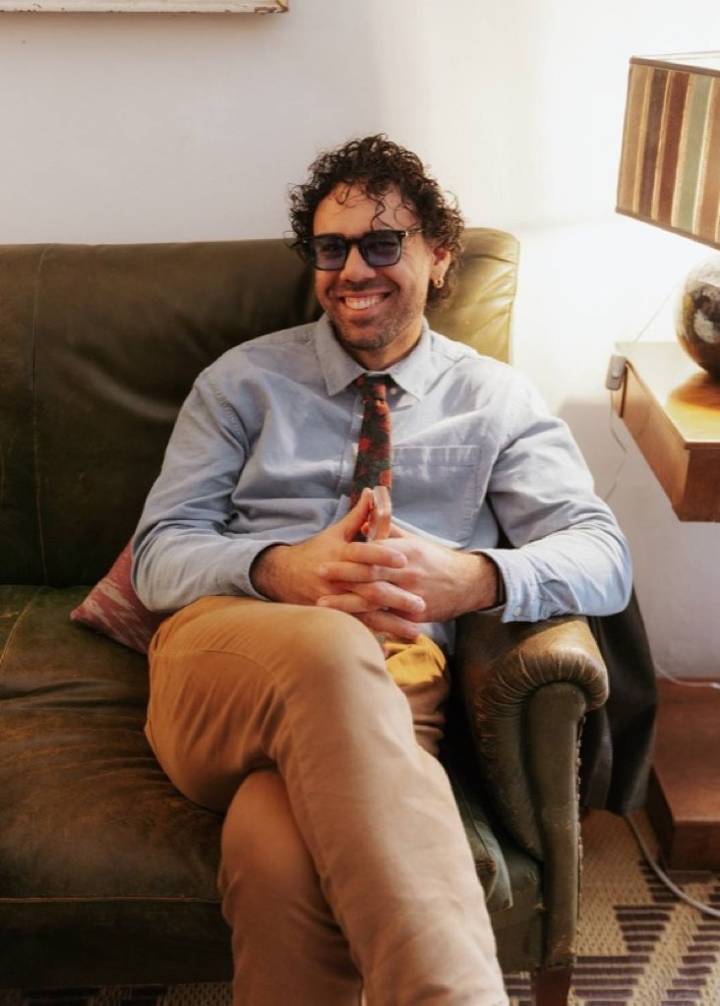 Paul Stavropoulos smiling, seated on a green leather couch